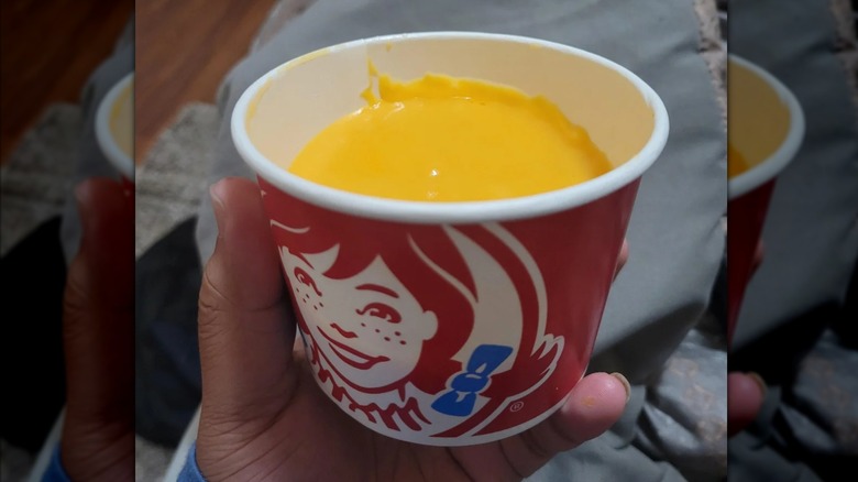 Hand holding a cup of Wendy's Swiss cheese sauce
