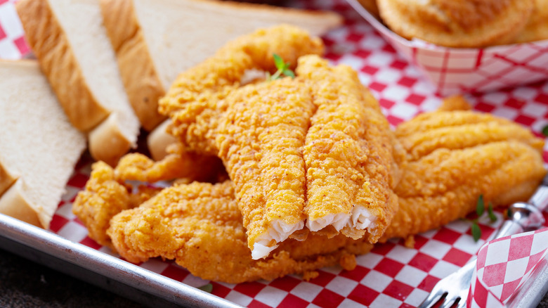 Fried catfish breaded Southern-style in cornmeal served on red-and-white checked paper with white bread as an accompaniment