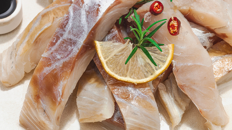 Raw pollock fillet portions garnished with a half lemon slice a sprig of rosemary and a tiny halved red chile pepper