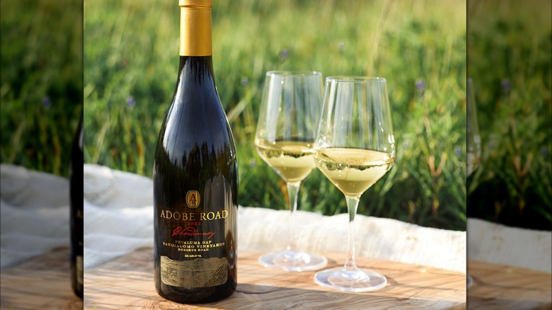 bottle of white wine with two glasses on a wooden board with green grass in the back