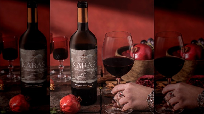 bottle of Karas Reserve Blend red wine with hand holding glass surrounded with pomegranates