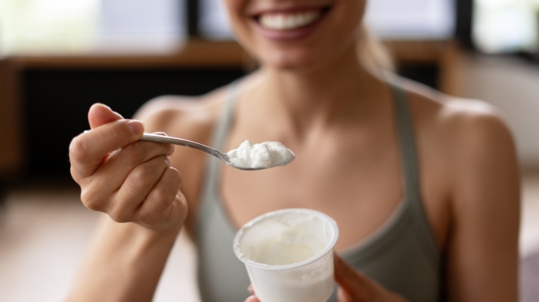 Woman smiling holding a pot of yogurt and a spoon