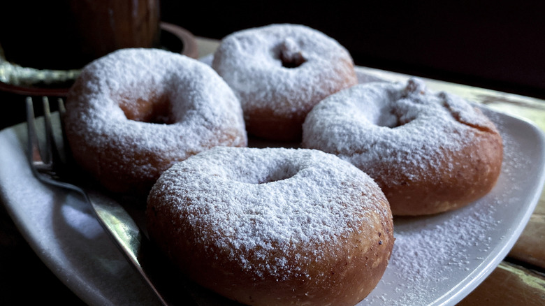 Four doughnuts topped with powdered sugar on a white plate