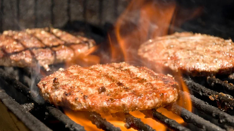 Several burger patties on a flaming grill