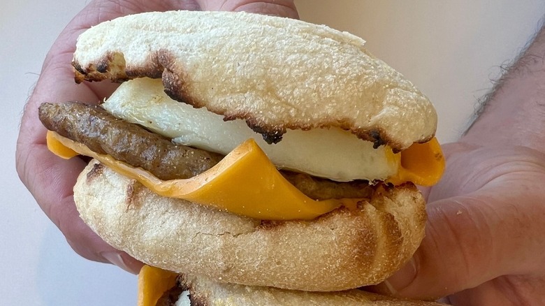 Someone holding two Sausage Egg McMuffins from McDonald's