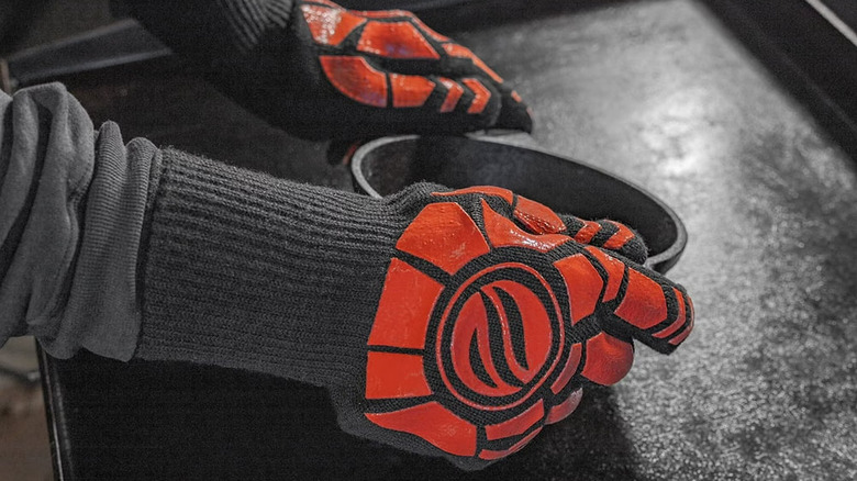 A person wearing Blackstone Griddle Gloves holding a hot cast iron pan