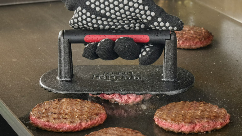 The Expert Grill Heavy Duty Cast Iron Griddle Press pressing burger patties on a grill