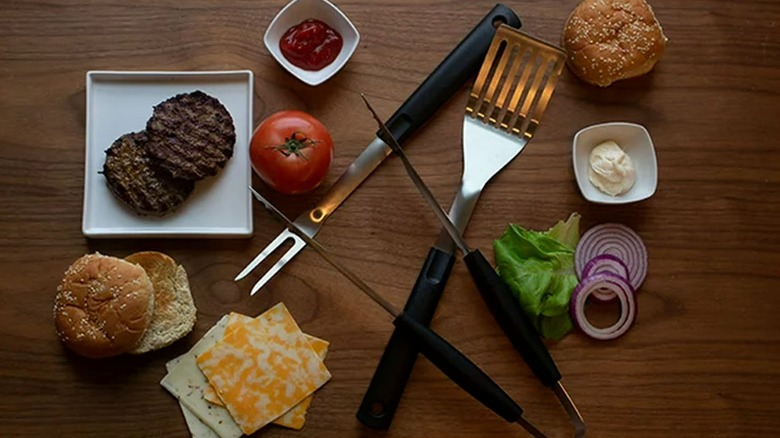 The Mainstays grilling tools on a table with burger fixings all around