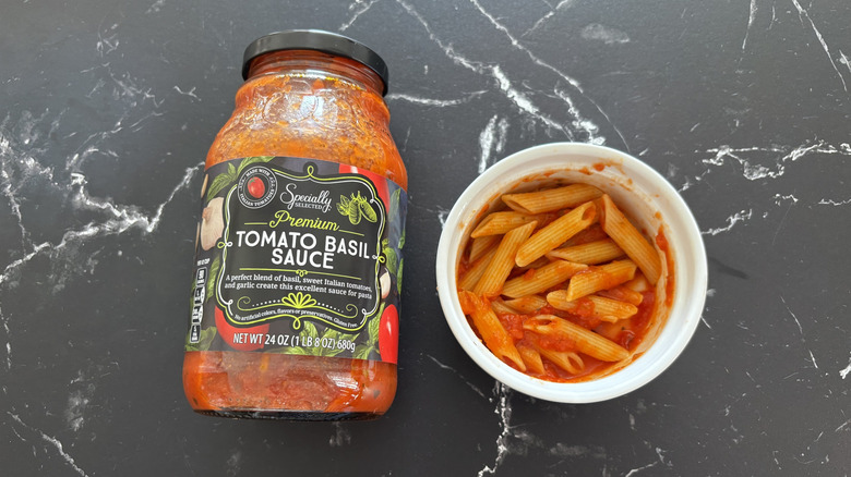 Aldi tomato basil pasta sauce jar next to bowl of pasta on marble