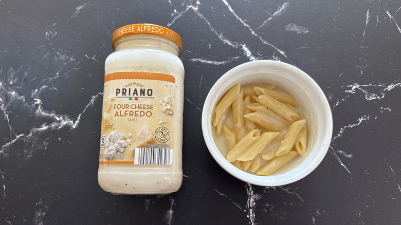 Aldi four cheese Alfredo sauce jar next to Alfredo pasta in bowl on a marble background