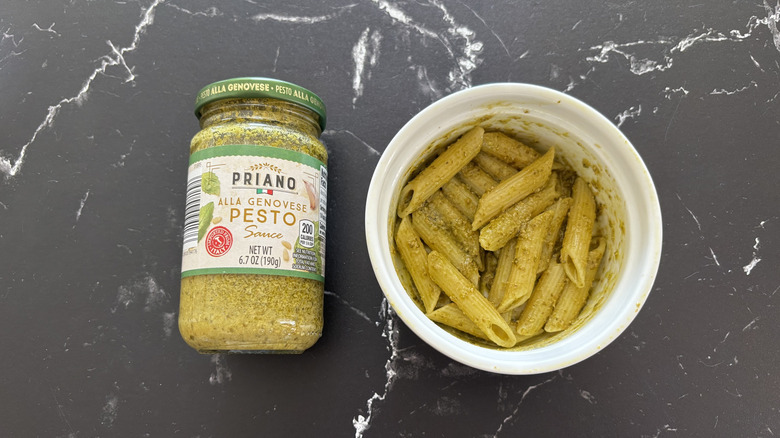 Aldi pesto sauce in jar next to pesto pasta in bowl on a dark marble counter