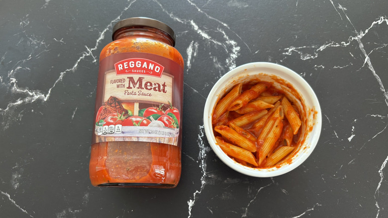 Aldi meat pasta sauce jar next to pasta in bowl on a marble counter