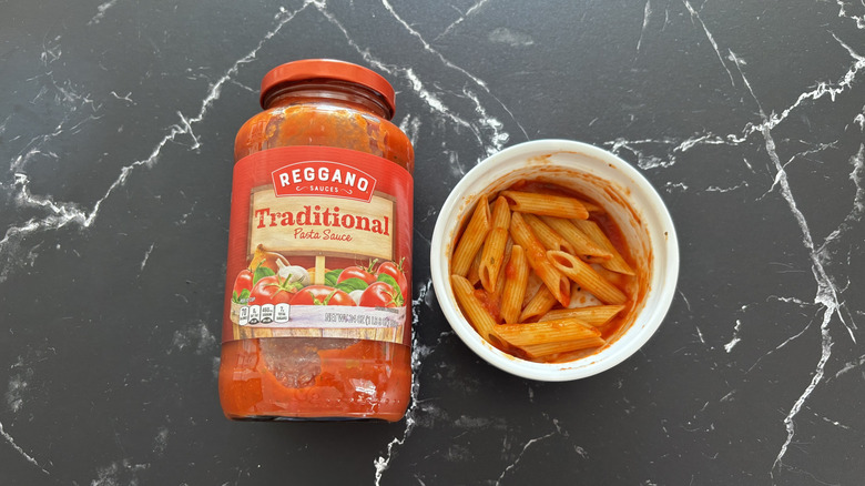Aldi traditional pasta sauce jar next to pasta in bowl on a counter