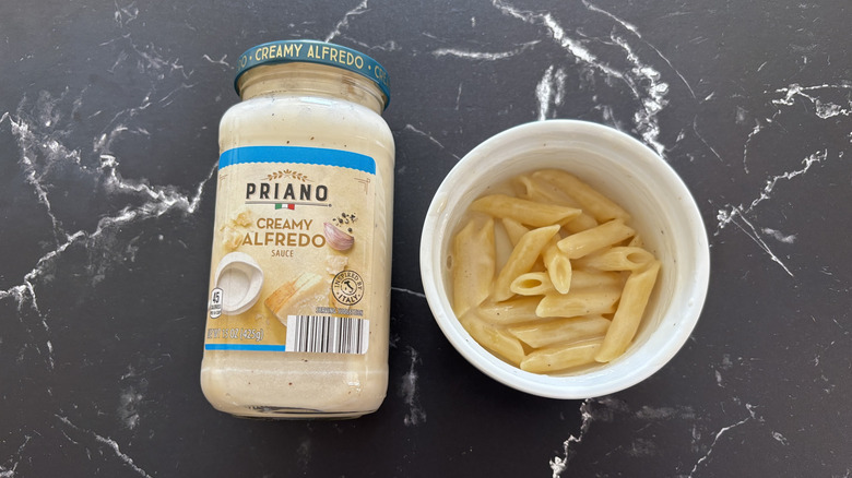 Aldi creamy Alfredo sauce jar next to Alfredo pasta in bowl on a dark countertop