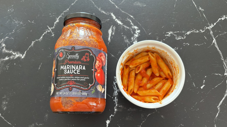 Aldi marinara sauce jar next to pasta in bowl on marble