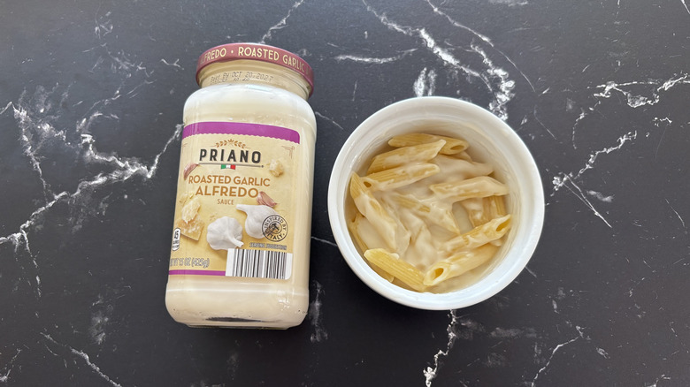 Aldi roasted garlic Alfredo sauce jar next to Alfredo pasta in bowl on a dark countertop