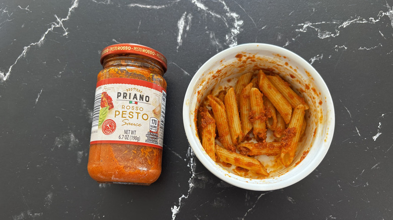 Aldi rosso pesto sauce jar next to red pesto pasta in bowl on a dark countertop