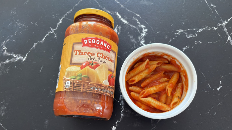 Aldi three cheese pasta sauce jar next to pasta in bowl on marble