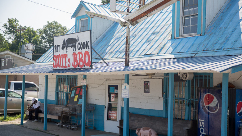 The storefront of Scott's BBQ, with a man sitting on a bench outside