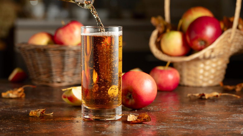 Apple cider poured from a bottle with apples in the background