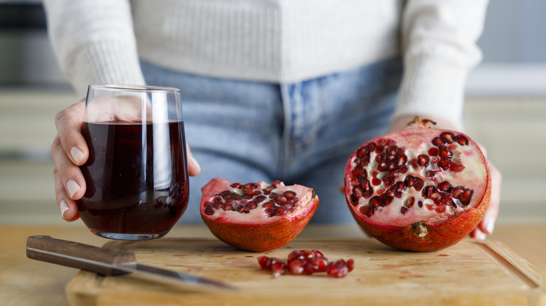 Woman holding a glass of pomegranate juice next to whole fruit