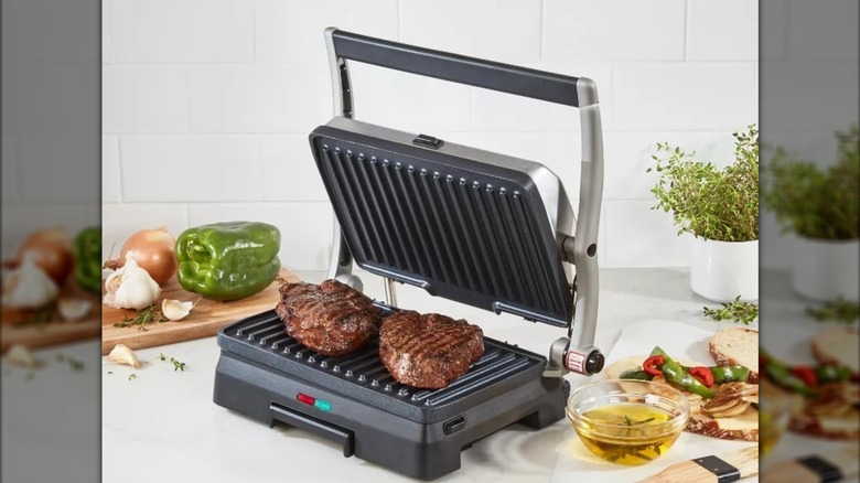 Cuisinart griddler grill and panini press with two steaks on countertop with ingredients