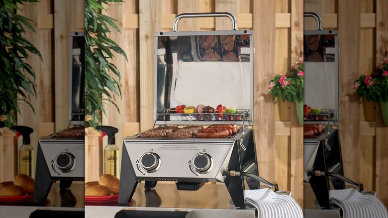 Expert Grill stainless steel 2-burner tabletop gas grill outdoors with kebabs, hamburgers, and hotdogs grilling