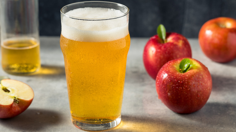 Hard apple cider in a glass next to real apples