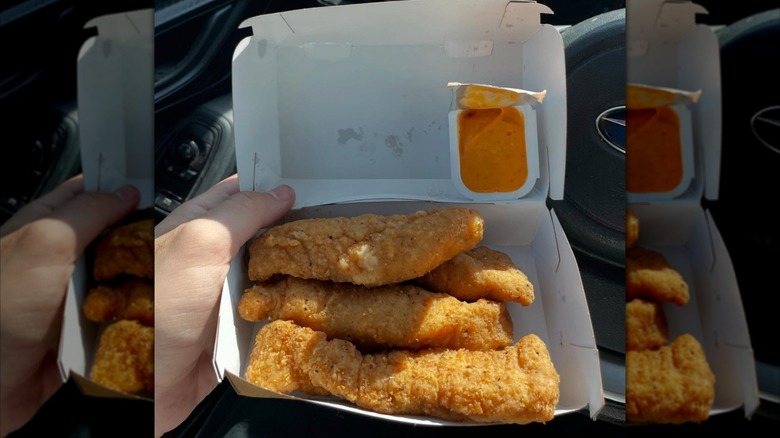 Open container of the McCrispy Strips with an open sauce cup resting in the lid