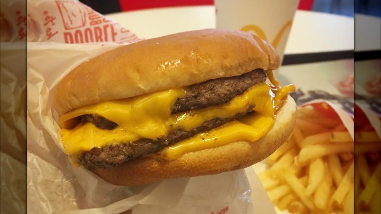 Someone holding a triple cheeseburger from McDonald's with fries and a drink