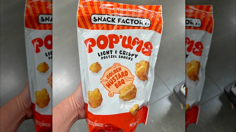 Hand holding an orange and white package of Pop'ums Golden Mustard BBQ