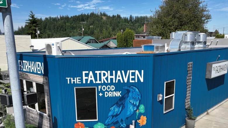 The Fairhaven blue building exterior with a raven mural with pines in the back