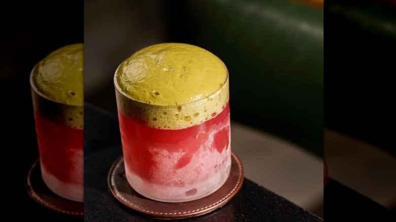 Cocktail in a frosted rocks glass, red juice on the bottom topped with a pea-green foam