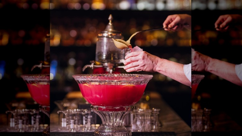 Hand dipping a ladle into a punch bowl of bright red liquid, pouring the cocktail into a glass of ice