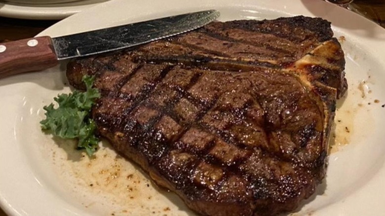 T-bone steak on white plate with a sprig of parsley and knife beside