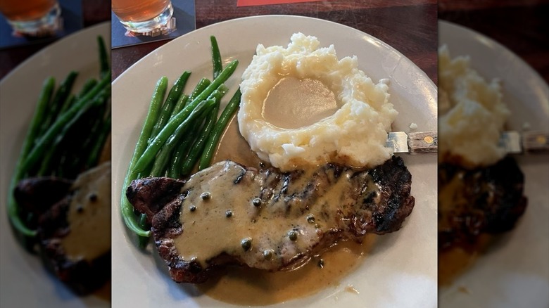 Gaelic steak with peppercorn sauce next to mashed potatoes with gravy and green beans on white plate