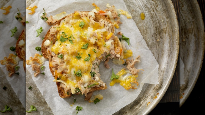 Top view of an open-faced tuna melt garnished with green herbs and served on parchment paper on a gray serving plate