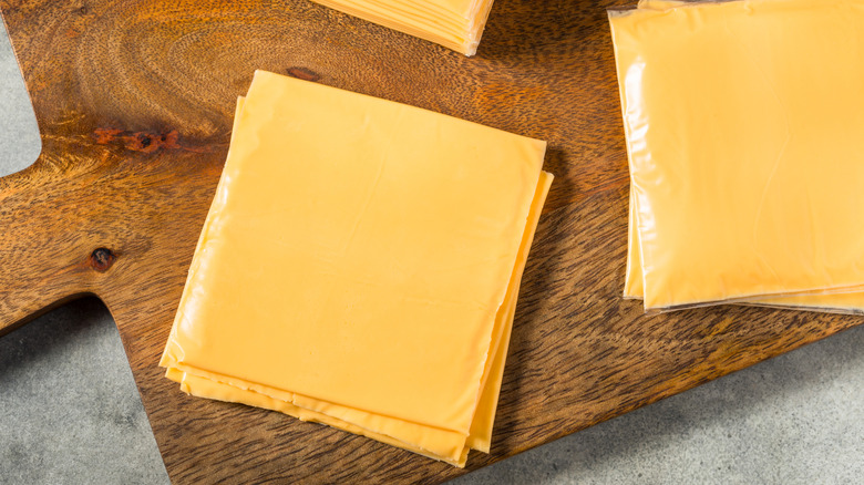 Slices of wrapped and unwrapped American cheese on a wooden cutting board