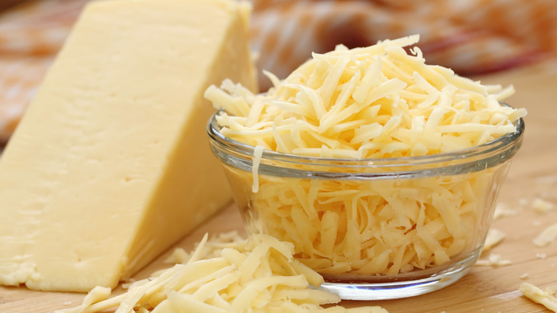 Shredded cheese in glass bowl with the whole block in the back