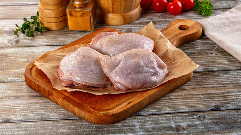 Raw chicken thighs on wooden board