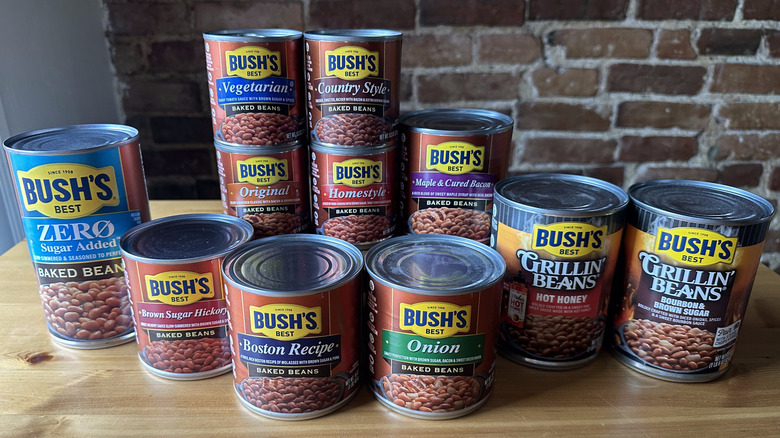 Cans of Bush's baked beans on wooden table against brick background
