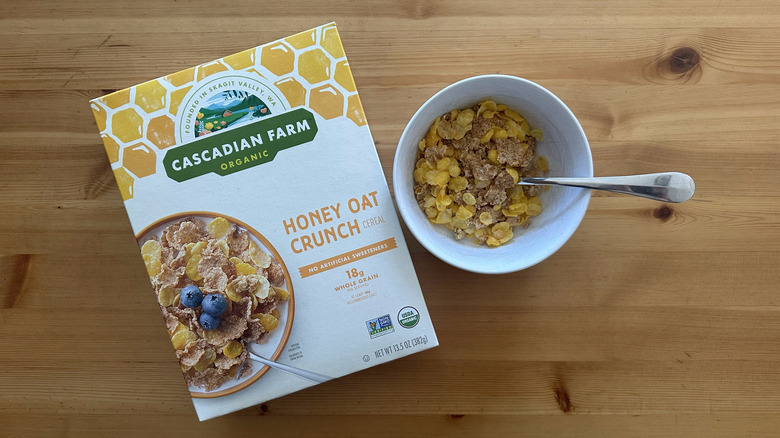 Top view of Honey Oat Crunch Cereal in a white bowl on table with the box next to it
