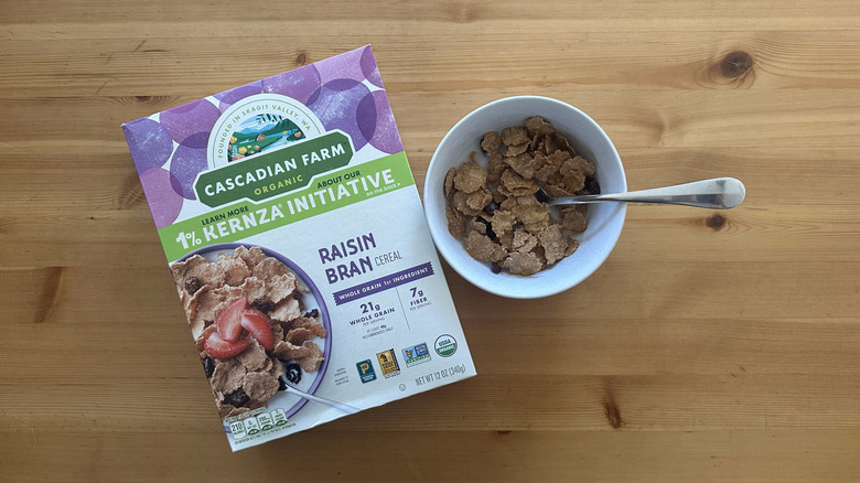 Raisin Bran Cereal box with some cereals mixed with milk in white bowl on table