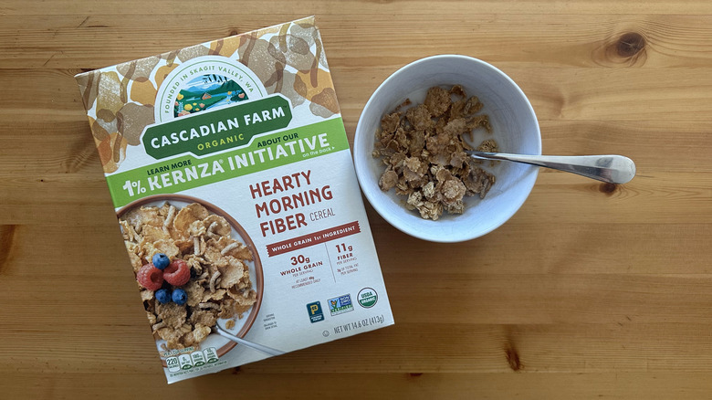 Cascadian Farm Hearty Morning Fiber Cereal box with some cereals served with milk in white bowl on table
