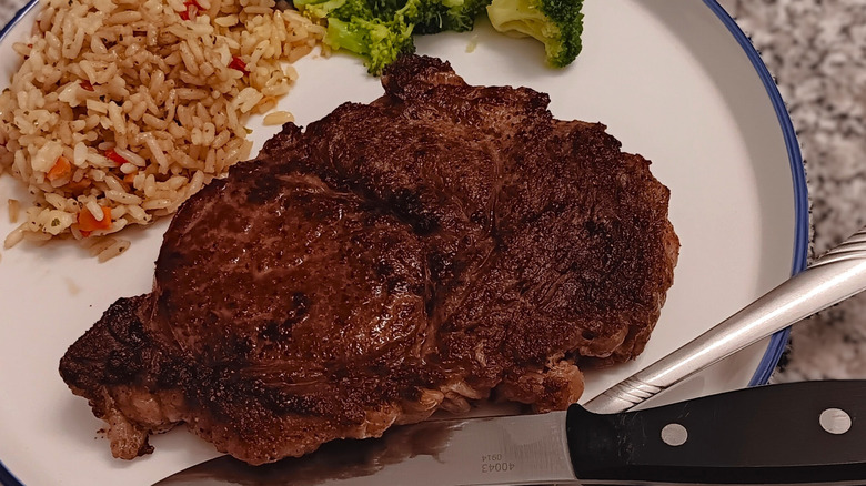 seared boneless ribeye with rice and broccoli on blue-trimmed white plate with silverware