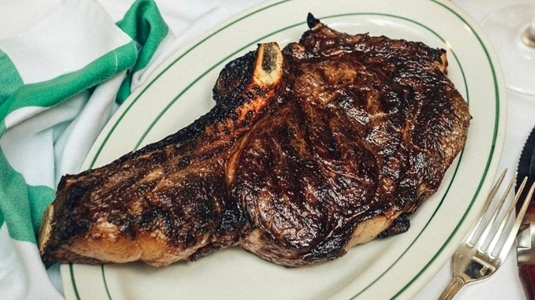 grilled tomahawk ribeye on oval platter with green trim and silverware