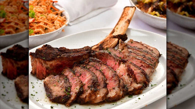 seared tomahawk ribeye sliced on plate with bone and sides