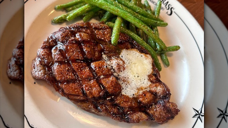 grilled boneless ribeye topped with melted butter with green beans on white plate