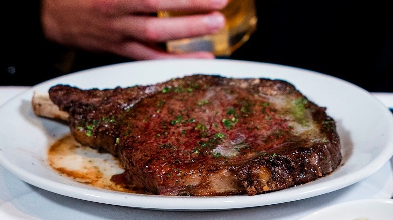 seared bone-in ribeye topped with herbs on white plate