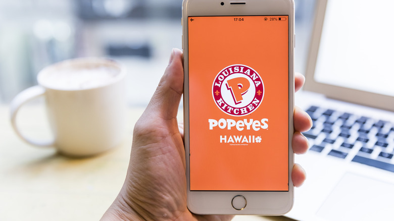 Hand holding a phone with the Popeyes app on the screen